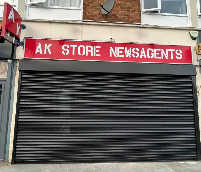 Black roller shutter protecting AK Store Newsagents